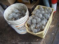 Two containers filled with small clear incandescent light bulbs with standard screw bases, dusty and used condition.