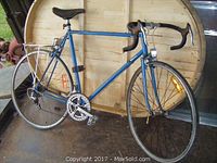 Side profile of blue vintage 12-speed road bicycle with rear carrier and 25-inch tires showing wear and age.