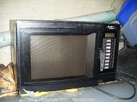 Black Amana commercial microwave showing front door with mesh window and multiple control buttons on the front panel including a handle on the right.