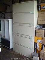 Front view of the full 5-section filing cabinet showing the closed lift doors and drawers, surrounded by boxes and other storage items.