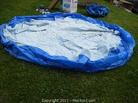 Deflated blue inflatable pool with a light blue and white liner spread on grass, showing its size and wear.