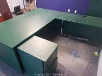 Green office desk and extension forming an L-shape with matching green two-drawer filing cabinet underneath. Floor area shown with some cables.