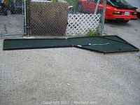 Two-piece wooden indoor putting green laid flat on ground with green artificial turf and black edging, showing overall layout and connection point.