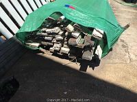 Top view of bundled reclaimed wood trim covered partially by green tarp, showing the ends of numerous overlapping pieces.