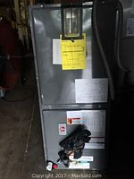 Full view of Rheem electric furnace showing gray metal casing, control panel, attached electrical conduit, and warning labels.