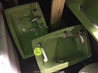 Photo of two reclaimed mid-century modern green Kohler bathroom sinks with chrome fixtures, shown leaning in storage.