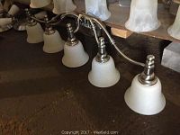 Photo shows the 5-light wall sconce laying flat, highlighting the brushed nickel finish and frosted glass bell-shaped shades.