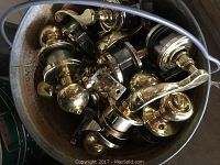 Close view inside a bucket showing many brass lever style passage knobsets with shiny finish and latch mechanisms.