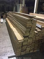 Stack of reclaimed 1×6 lumber boards of varying lengths in a warehouse setting.