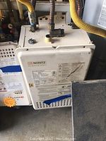 Front view of white Noritz tankless water heater with visible connections and labels.