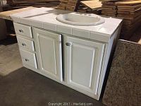 Photo of white reclaimed bathroom base cabinet with tile countertop and overmounted round sink, showing three drawers on the left and two cabinet doors under the sink area.