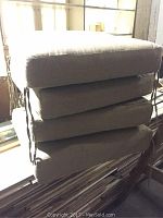 Photo shows four stacked beige outdoor patio furniture cushions in rectangular shape with piped edges.
