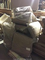 Photo of four square beige outdoor patio furniture cushions wrapped in plastic, stacked together indoors.