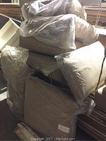 Four new beige outdoor patio cushions individually wrapped in clear plastic, stacked for display.