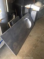 Photo showing the dark granite countertop leaning against a wall with undermount white ceramic sink installed and chrome faucet fixtures visible.