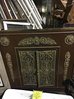 Front view of brass decorative fireplace mantle screen showing central hinged doors and ornate cutwork against wooden backdrop
