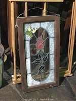 Photo of rectangular leaded stained glass window panel with a rose and two butterflies design framed in dark wood, with hanging wire attached.