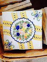 Photo shows one of the square antique French kitchen tiles with detailed floral design and yellow arch patterns, showcasing its style and condition.