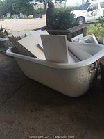Side view of white enamel clawfoot tub with chipping paint, filled with shelves, outdoors on concrete