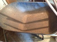 Close-up of large deep metal wheelbarrow showing rust on inside surface