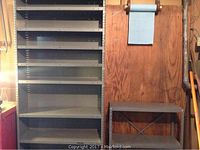 Four tall grey metal shelving units and one smaller two-tier shelf against wooden wall in garage or workshop area