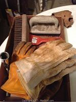 Photo showing four pairs of heavily used leather gloves along with five wire brushes arranged on a surface.