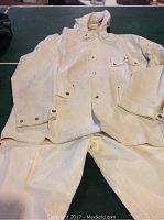 White Coleman PVC rain jacket and pants laid flat on green surface