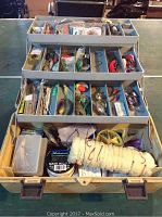 Open fishing tackle box displaying multiple tiers with various fishing lures, spools of fishing line, and accessories.