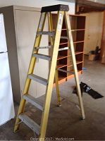 Yellow fiberglass step ladder standing open in basement area with white appliances and wooden shelving.
