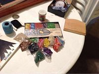 Wooden carrying case on table with assorted colored sand packets in various colors, spool of blue twine, and small black container with tape and rubber bands.