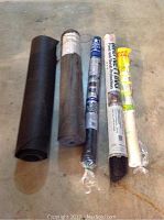 Five rolls of garden mesh coverings laid out on a floor including black, brown, white, and blue rolls wrapped in plastic