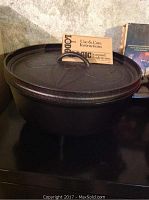 Heavy black cast iron Lodge Logic pot with lid on top, unopened use and care instructions visible.