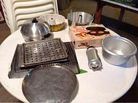 Photo showing the assorted bakeware including donut factory pan, bundt and angel food cake pans, cookie sheets, tray, and bun warmer all arranged on a round table.