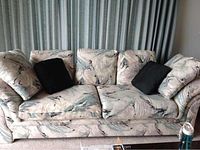 Front view of couch with patterned upholstery and black cushions under curtain background