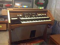 Front view of the Hammond organ showing two keyboards, drawbars, control switches, and roll-top cover partially open.