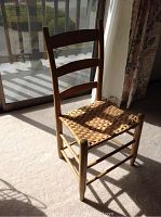 Wooden chair with woven cane seat in sunlight, showing front and side angles.