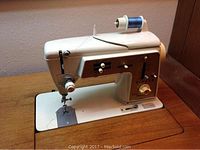 Close-up of white Singer sewing machine with blue thread spool on wooden desk.