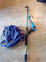 Photo showing an extendable green water blaster with a foam grip and adjustable blue nozzle alongside a blue flexible collapsible hose laid coiled on a floor surface.