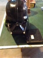 Darth Vader helmet and accompanying voice control box placed on a green table surface