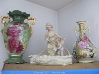 Photo showing both vases with floral designs and gold handles alongside large figurine of woman and child in boat