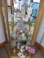 Display cabinet containing various ceramic figurines including 3 distinctive Snow Babies, lambs, sheep, a ceramic elephant, and other decorative figurines.