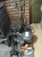 Photo showing black wrought iron fireplace tools with brass handles and stand, black iron kettle, two black dog figurines, black squirrel figurine, and painted fireman doorstop on a stone hearth