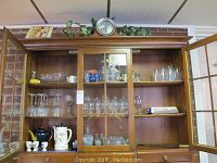 Wide view of glassware collection on shelves inside display cabinet including wine, sherry, cordial glasses and egg cups.
