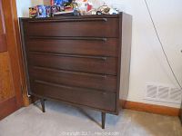 Front view of dark wood dresser with five drawers and items on top.