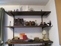 Wide view of shelves showing white ceramic religious figurines, three pairs of brass animal bookends, three small framed animal pictures, and a vintage glass dome clock.