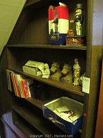 Shelf with lots including Uncle Sam metal bank, horse and wagon tanker metal bank box, children's books and various figurines.