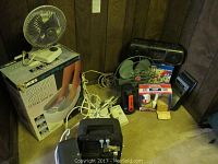 Overview of lot showing two fans, Panasonic 8 track player box, Bell and Howell projector, Bubble Bliss foot spa box, cassette player, extension cords.