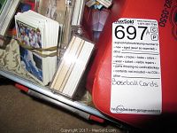 Stacks of loose baseball cards in rubber bands next to red hard case with lot tag
