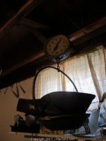 Antique Detecto hanging scale suspended near ceiling with a large metal scoop pan below and circular dial showing weight in pounds.
