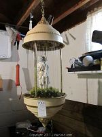 Full view of the hanging lamp showing the dome top and bottom with hanging strings enclosing the figurines and greenery inside.